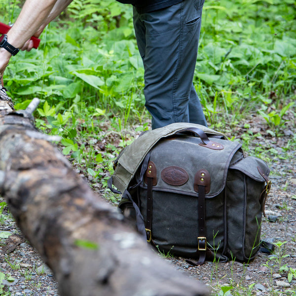 Nessmuk Pack sits on the ground next to a person sawing a tree. 