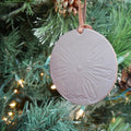 Brown leather ornament with snowflake imprint hangs in a Christmas tree. 