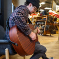 Person plays a guitar sitting in a chair with a handmade leather black guitar strap. 
